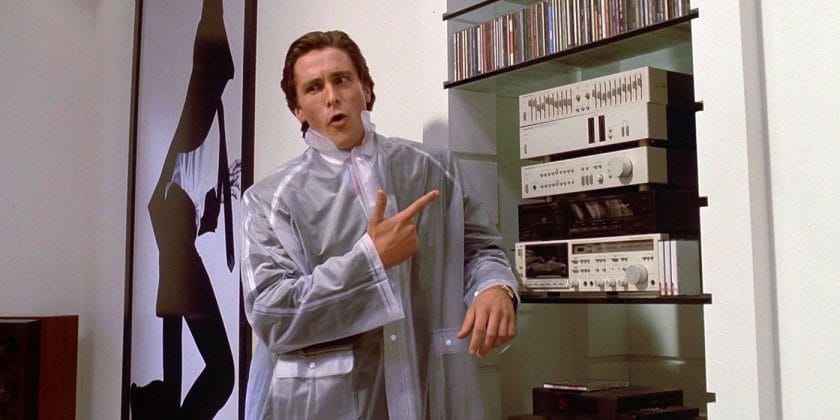 Patrick Bateman in American Psycho wearing a sheer rain slicker and pointing towards his stereo